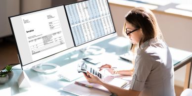 Woman analyzing financial documents with multiple screens and calculator.