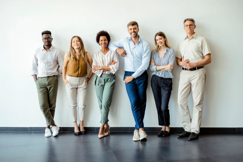 Group portrait of happy business people in smart casual outfits posing against office wall background. Smiling and looking at camera