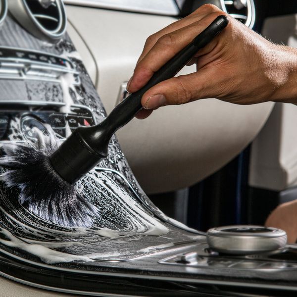 A hand cleans a car dashboard with a brush and soap.