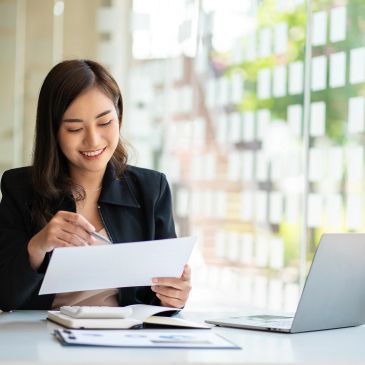 Smiling woman reviewing documents at desk.