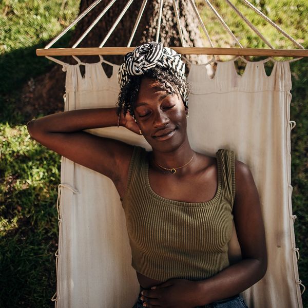 Young woman with a black and white head wrap over zigzag curls lounging in a beige hammock under a t
