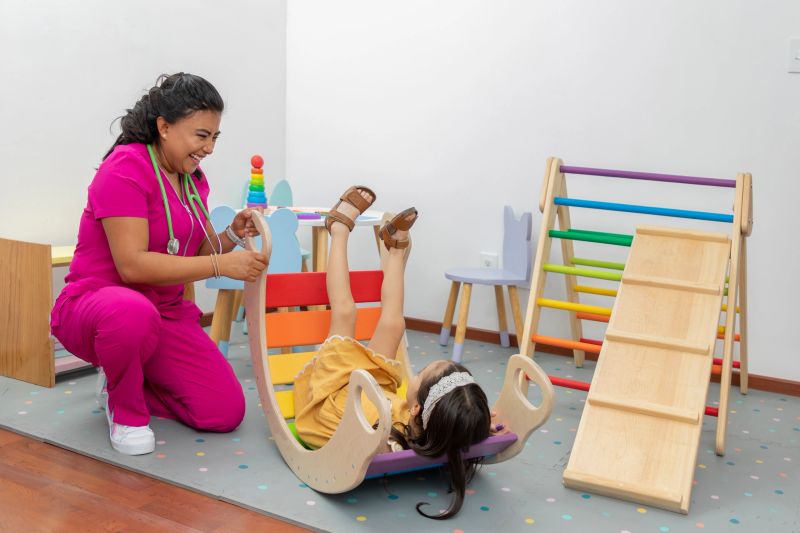 Latina pediatric doctor, laughing while playing with a girl in the play area of her office .