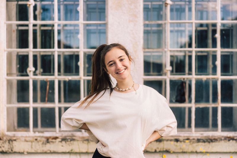 Young fashionable woman with ponytail wearing property released handmade craft designer T-Shirt Standing looking towards the Camera. Majestic industrial Window in the background. Millennial Generation Girl Young Fashion Design Portrait. Nontrivial