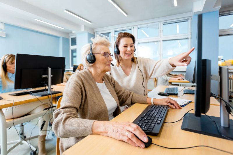 Smiling female manager explaining senior trainee using computer at desk in office