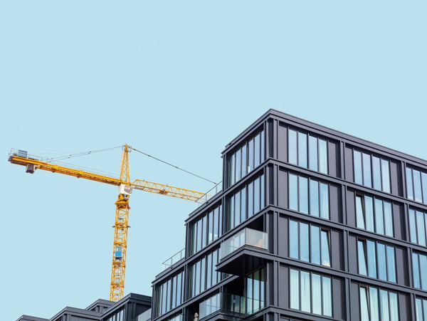 Modern glass building with a yellow construction crane against a clear sky.
