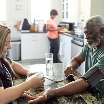 A healthcare worker checks blood pressure of an elderly man at home.