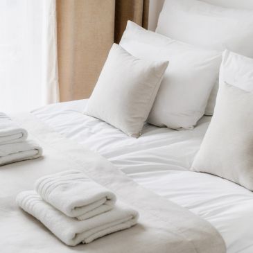 Neatly made bed with white linens and folded towels.