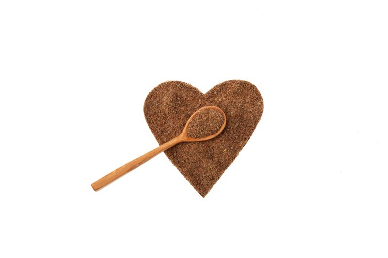 Milk Thistle Oil cake or Silybum marianum extract in heart shape and wooden spoon on white background. Herbal superfood for aiding liver function. Strong antioxidant.
