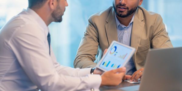 Two businessmen discussing data charts on a tablet in an office.
