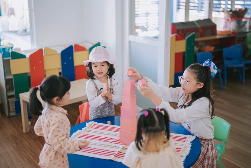 Asian female Montessori preschool student finishing top up toy block playing in classroom