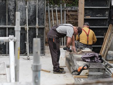 Two construction workers at a building site using tools.