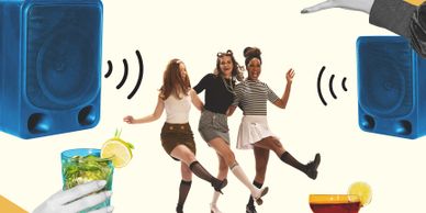 Three women dancing joyfully between two large speakers with cocktails in hands.