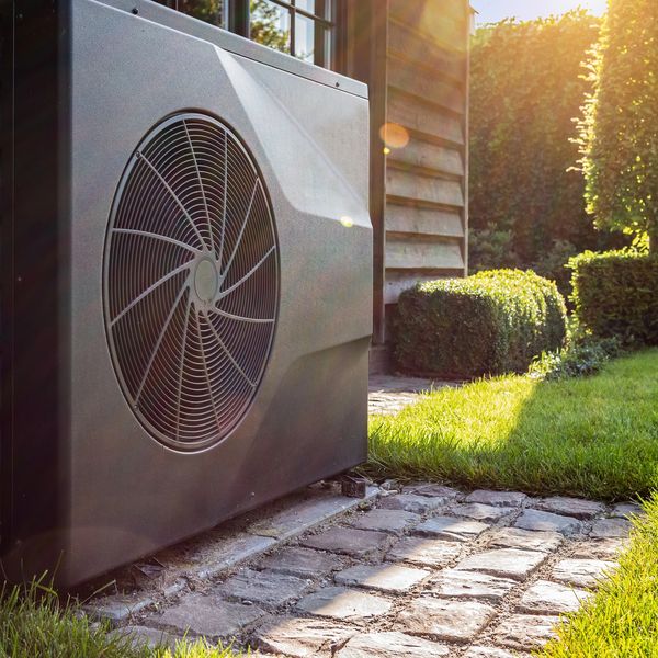 Outdoor heat pump unit beside a garden with sunlight.