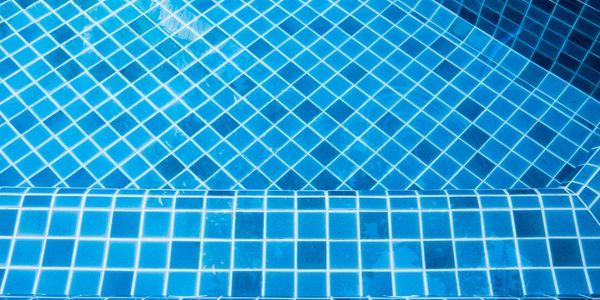 Close-up of blue tiled pool steps with water reflections.