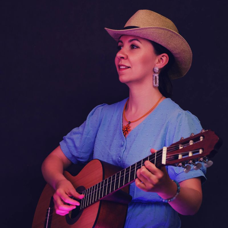 Portrait of a woman with a guitar in her hands on a black studio background. A female musician in a blue dress and a straw hat with an acoustic wooden guitar