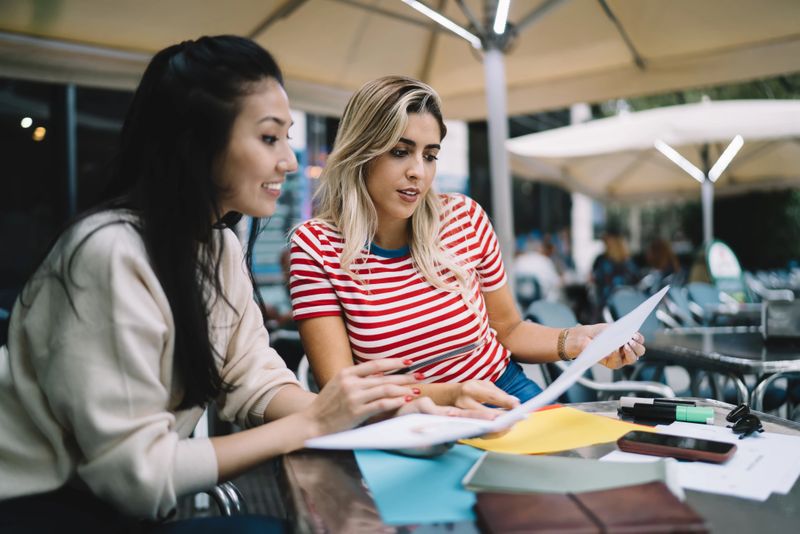 Diverse remote colleagues have brainstorming meeting for analyzing documents during paperwork in street cafeteria, young female students preparing to college tests togetherness studying info outdoors