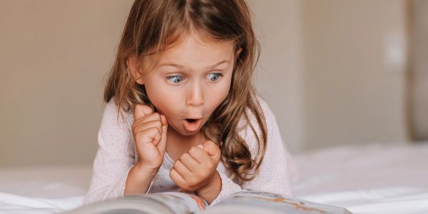 A young girl with an amazed expression reading a book.