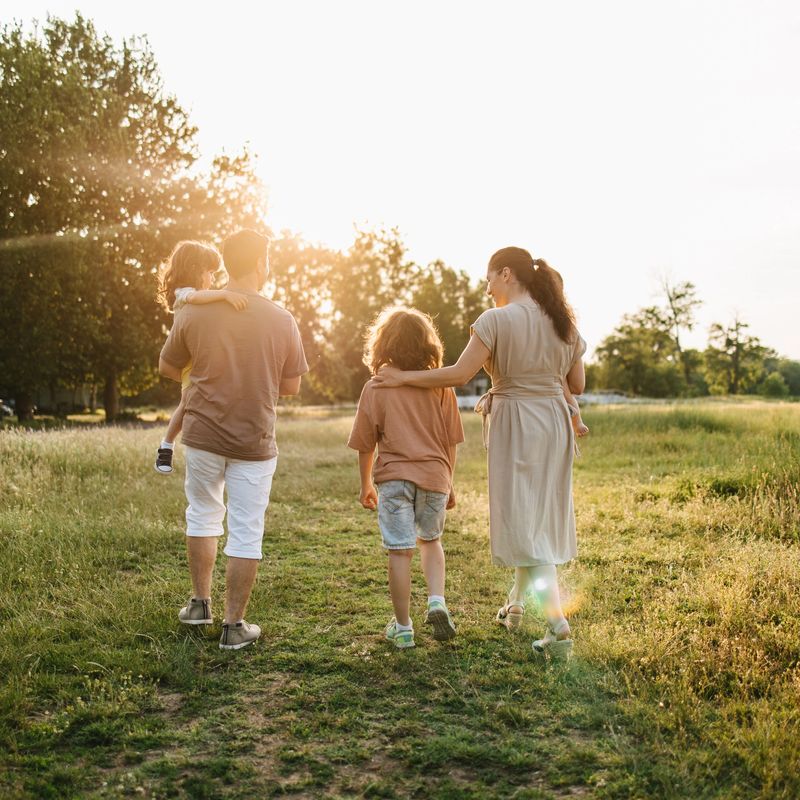 Rear view of family with three children walking on grass field during sunset.