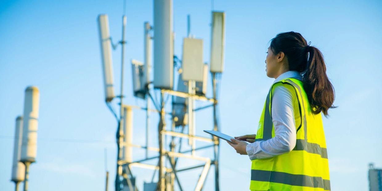 Engineer inspecting telecommunications tower with tablet.