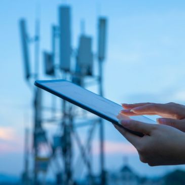 Person using tablet near telecom towers at dusk.