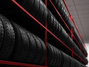 Rows of black tires neatly arranged on red metal racks in a store or warehouse.