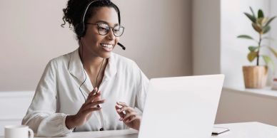Woman wearing headphones and glasses video chatting on a laptop.