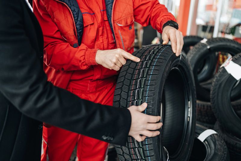 Young handsome customer after fueling his car on gas station looking for some good new winter tires. He is talking with salesman and asking him for advice.