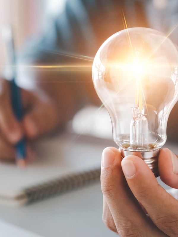 A person holding an illuminated light bulb in their hand.
