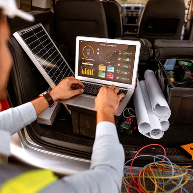Persona revisando datos de consumo de energía en una laptop junto a un panel solar.