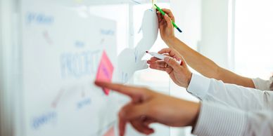 People collaborating on a project plan using sticky notes and markers on a whiteboard.