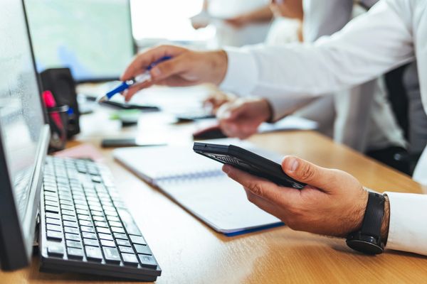 Person using calculator at desk with laptop and notebook.
