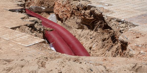 Red pipes being installed in a dug trench on a construction site.
