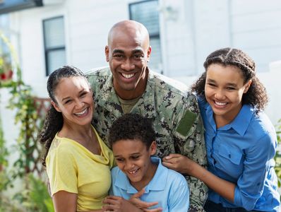Smiling military man embraces his happy family outdoors.