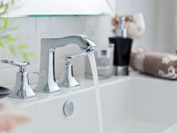 Modern chrome faucet with water running in a clean bathroom sink.