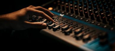 Hand adjusting knobs on a sound mixer in a dimly lit room.
