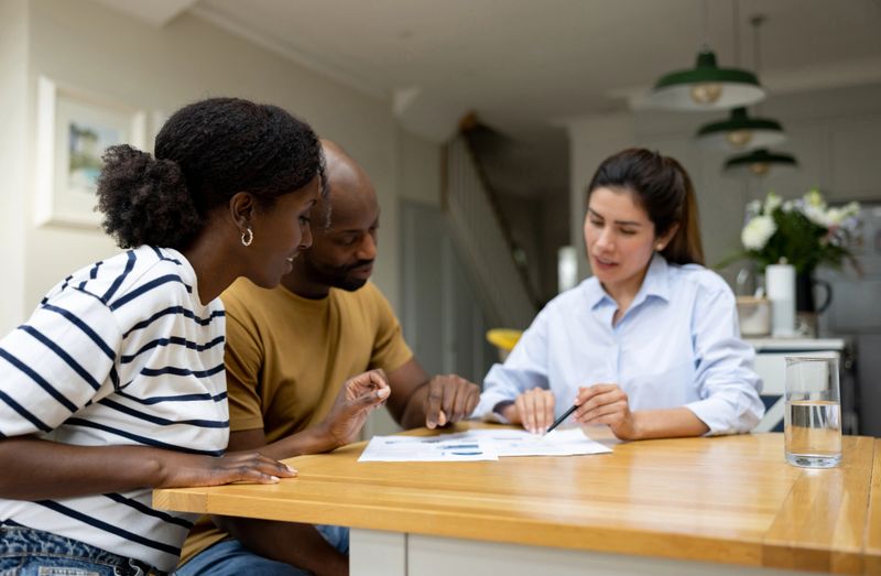 African American couple talking to a real estate agent and reviewing the paperwork while buying a house - home ownership concepts