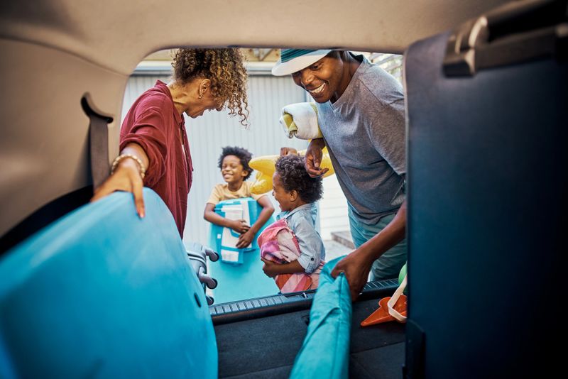 Excited black family packing their car for a trip to the beach. Cheerful parents and playful kids looking happy while loading their boot for a family vacation. Time to travel and have fun on holiday