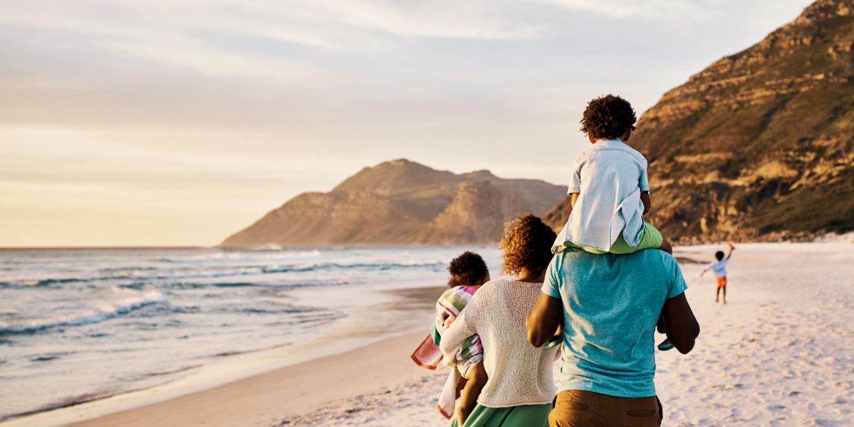 Family walking on the beach during sunset with mountains in the background.
