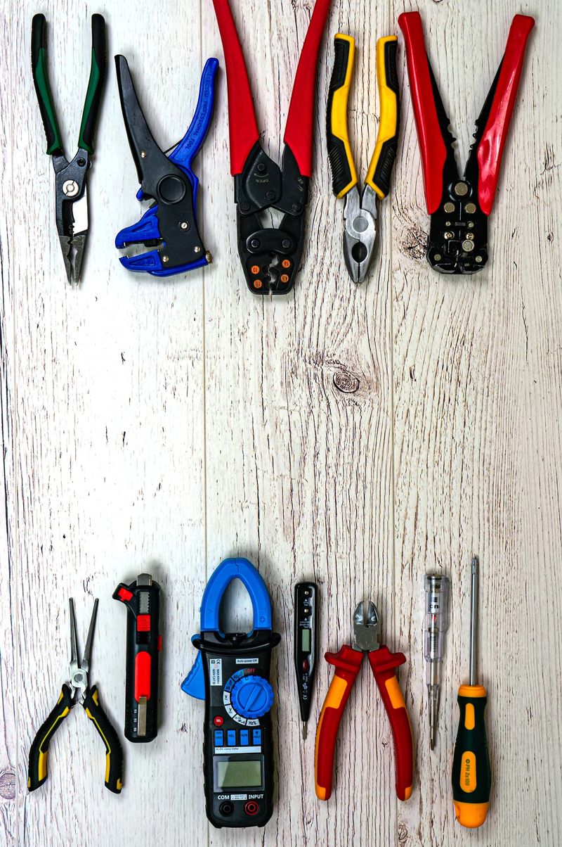 Professional electrician tools and electrical components on light wooden boards. Pliers, strippers, crimpers, multimeter, tester, screwdriver. Top view. Portrait orientation.