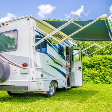 A person sitting in the doorway of a white RV with an extended green awning.
