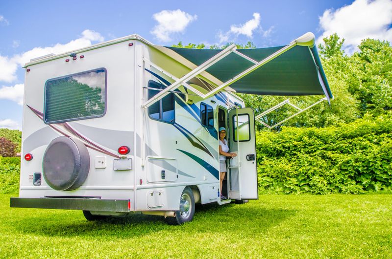 Woman getting out of small Class C motorhome on the grass with awning opened