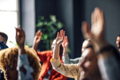People raising hands in a group setting, possibly voting or participating.