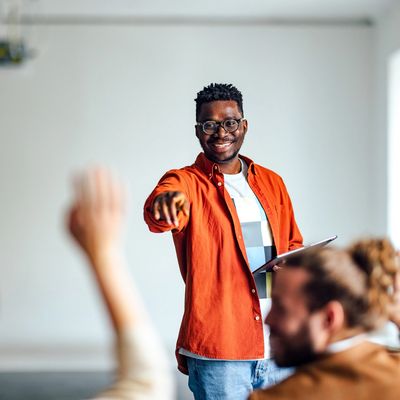 En smilende lærer som peker på en student som har rukket opp hånden