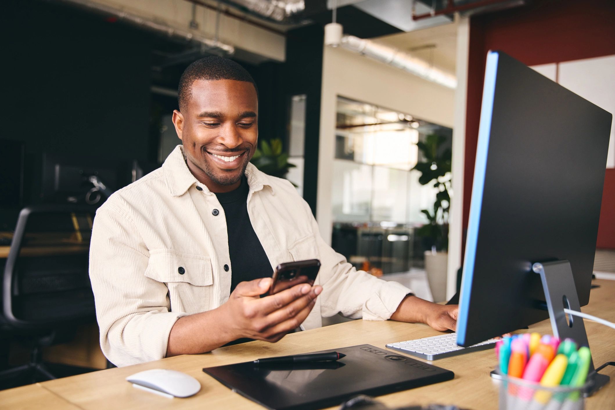 Smiling man checking his phone at a modern office desk.