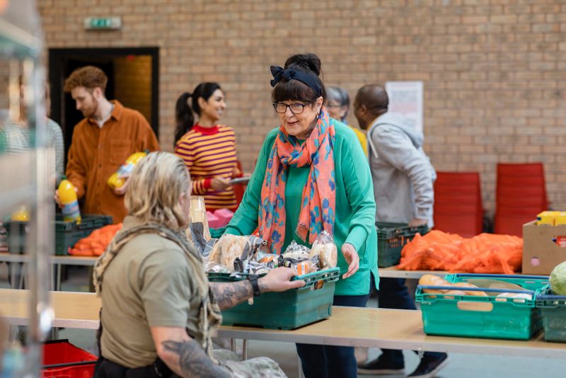 Group of volunteers organising food donations onto tables at a food bank in the North East of England. They are working together, setting up sections of the room in a church.