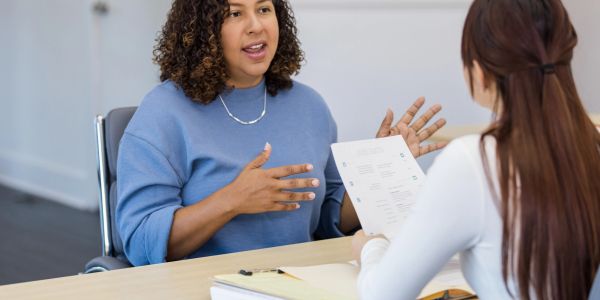Two women having a discussion, one holding a CV.