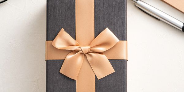 Elegant gift box with golden ribbon, surrounded by coffee, glasses, and pen.