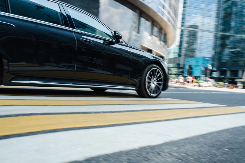 Black luxury car riding at the financial downtown district, blurred in motion. Low angle view on the road at crosswalk.