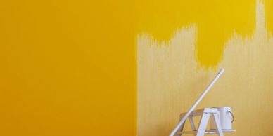 Wall partially painted yellow with ladder and paint can.