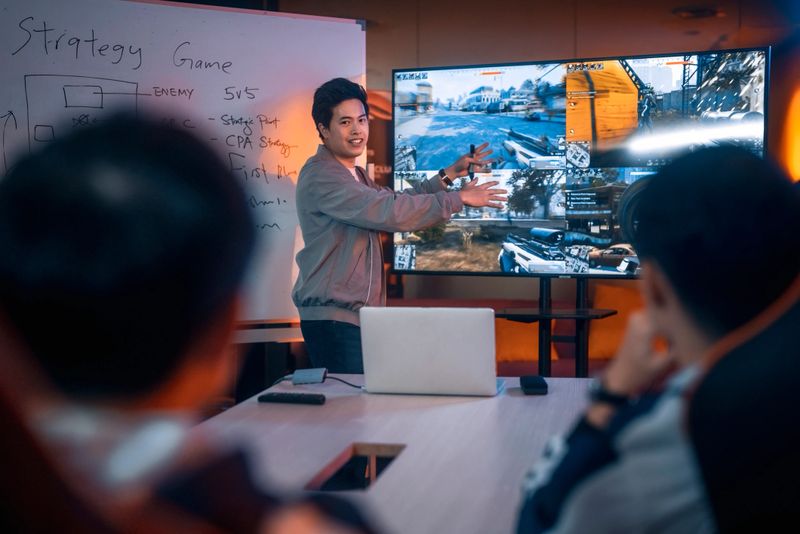 Asian Chinese Esport Team Coach analysing briefing strategy to team before grand final videogame competition in meeting room with white board and television